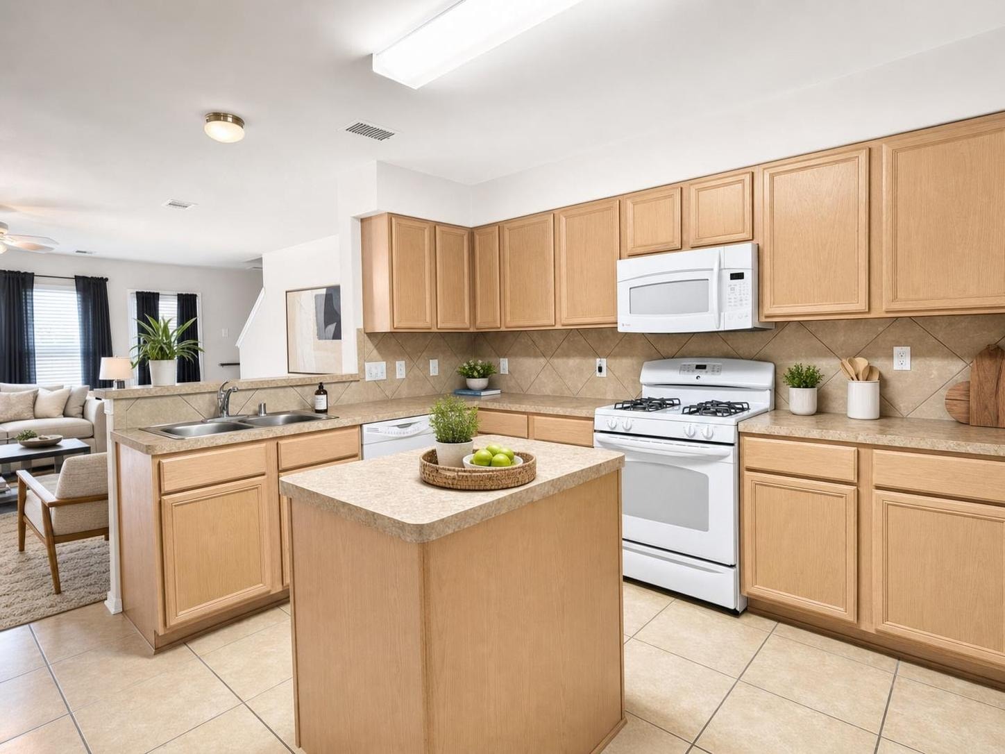Modern kitchen with light wood cabinets, beige tile floor, white appliances, and a small central island with plants and fruit.