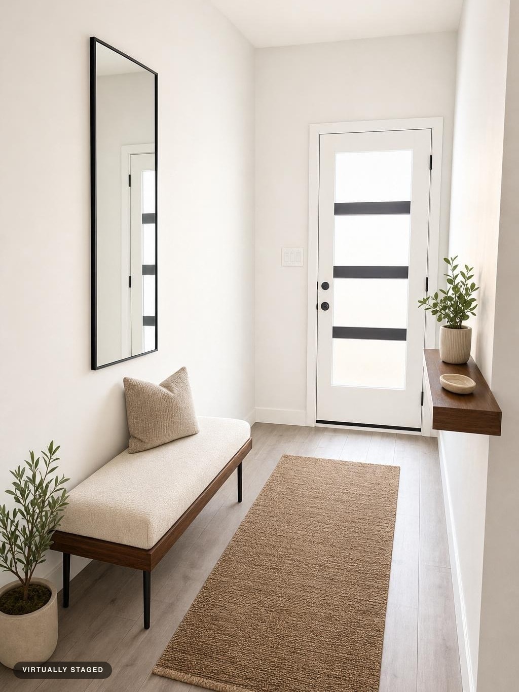 Minimalist entryway with cream bench, black-framed mirror, floating shelf with plant, tan rug, and potted plants by door.