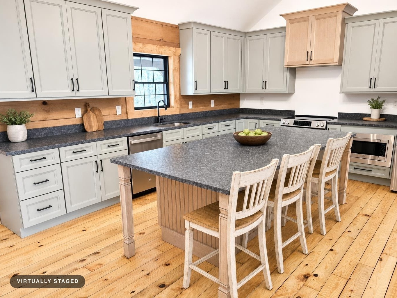 Modern farmhouse kitchen with gray cabinets, dark countertops, wood floors, and a large island with three distressed white chairs.