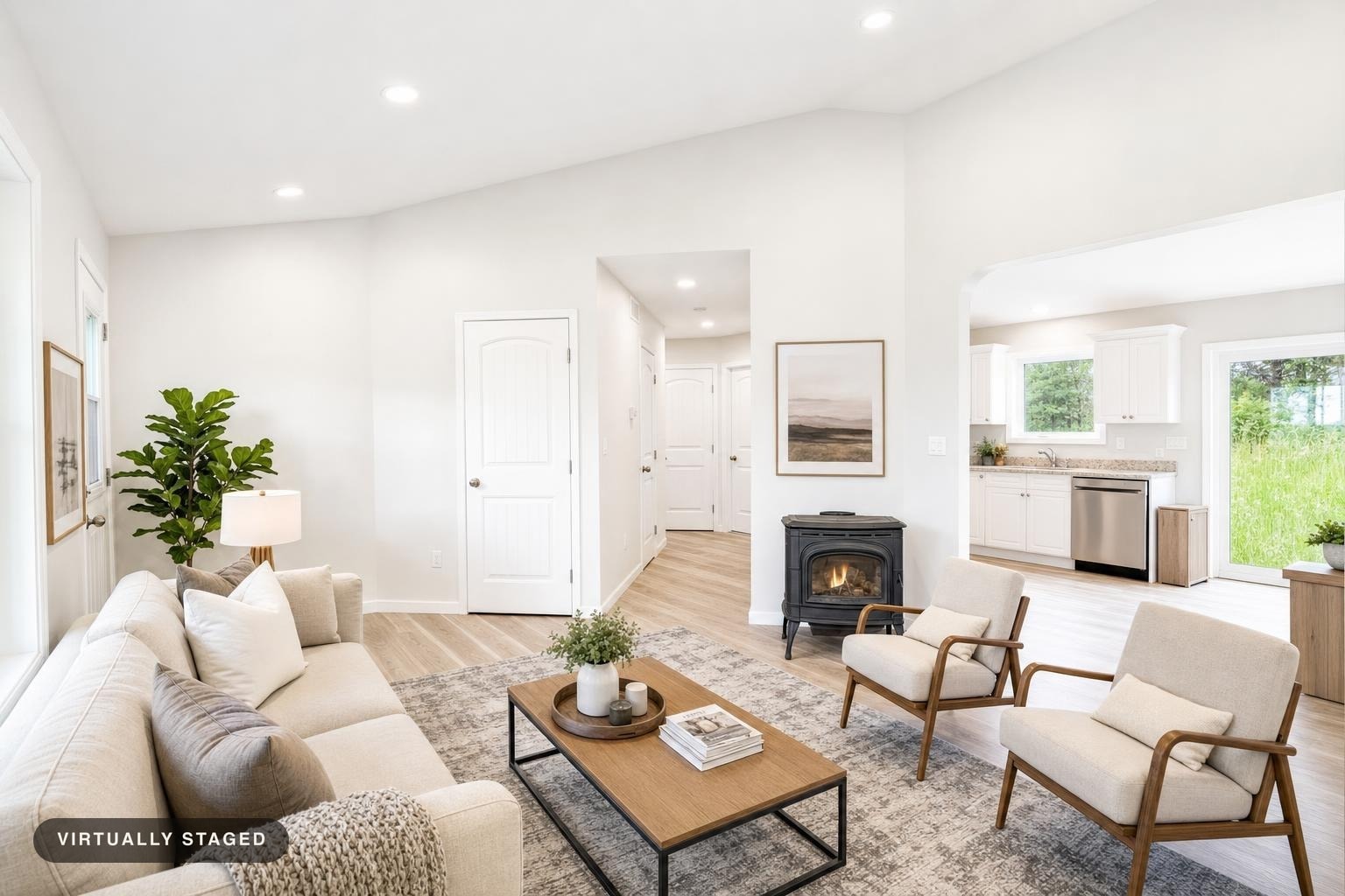 Bright modern living room with cream sofa, two beige armchairs with wood frames, black stove, wood coffee table, and light wood floors.