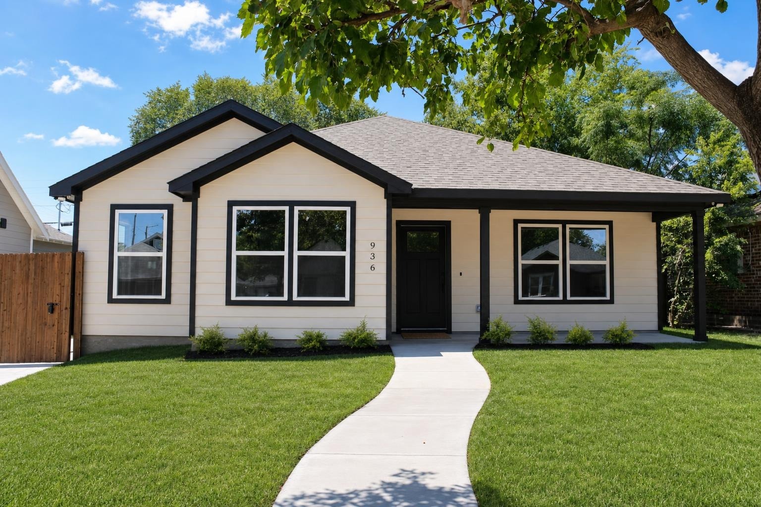 Single-story house with beige siding, black trim, black front door, three double-pane windows, front yard with green lawn and small shrubs.