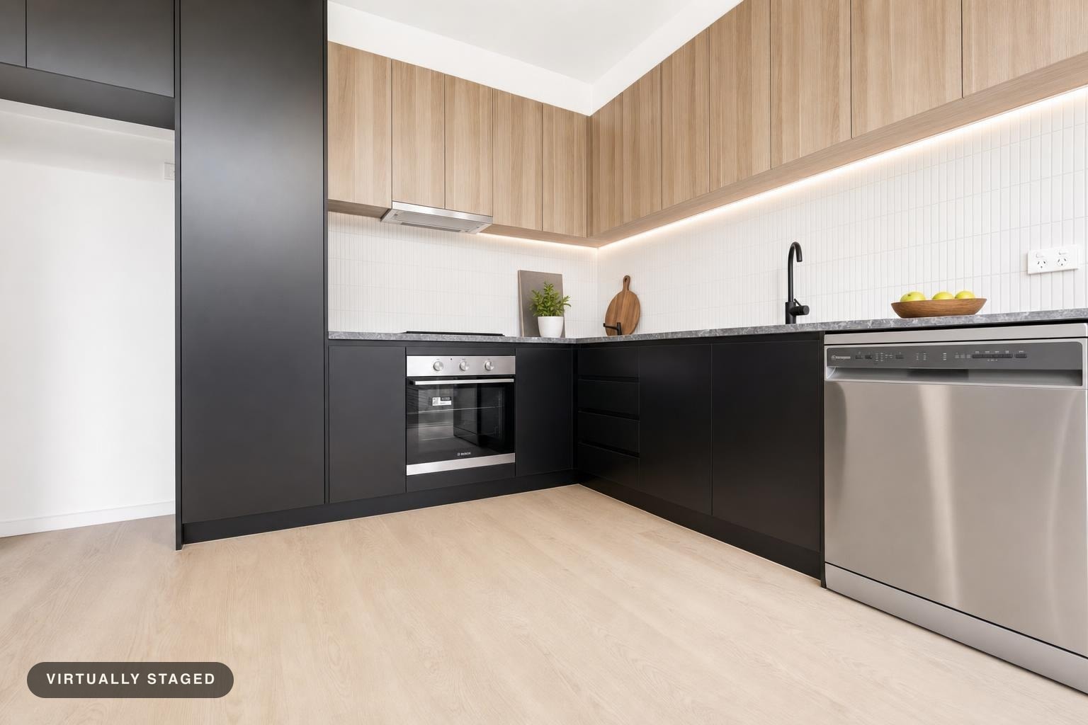 Modern kitchen with black lower cabinets, light wood upper cabinets, stainless steel oven and dishwasher, and light wood flooring.
