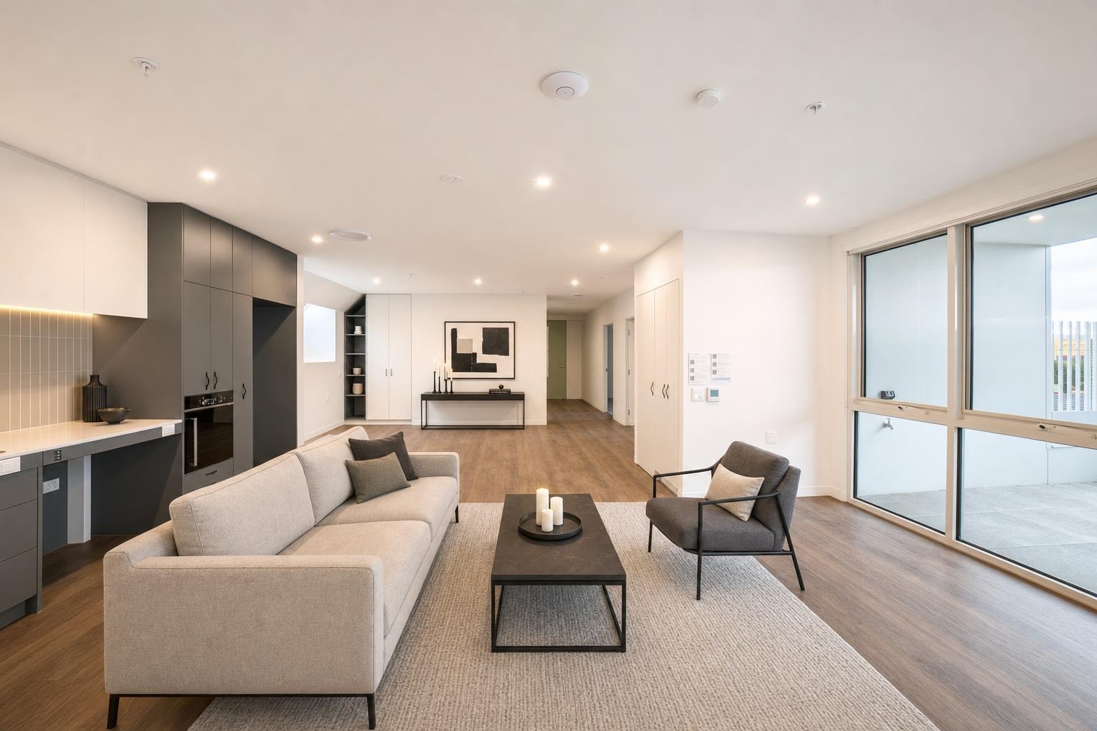 Modern living room with beige sofa, dark gray armchair, black coffee table, and large windows with light wood flooring