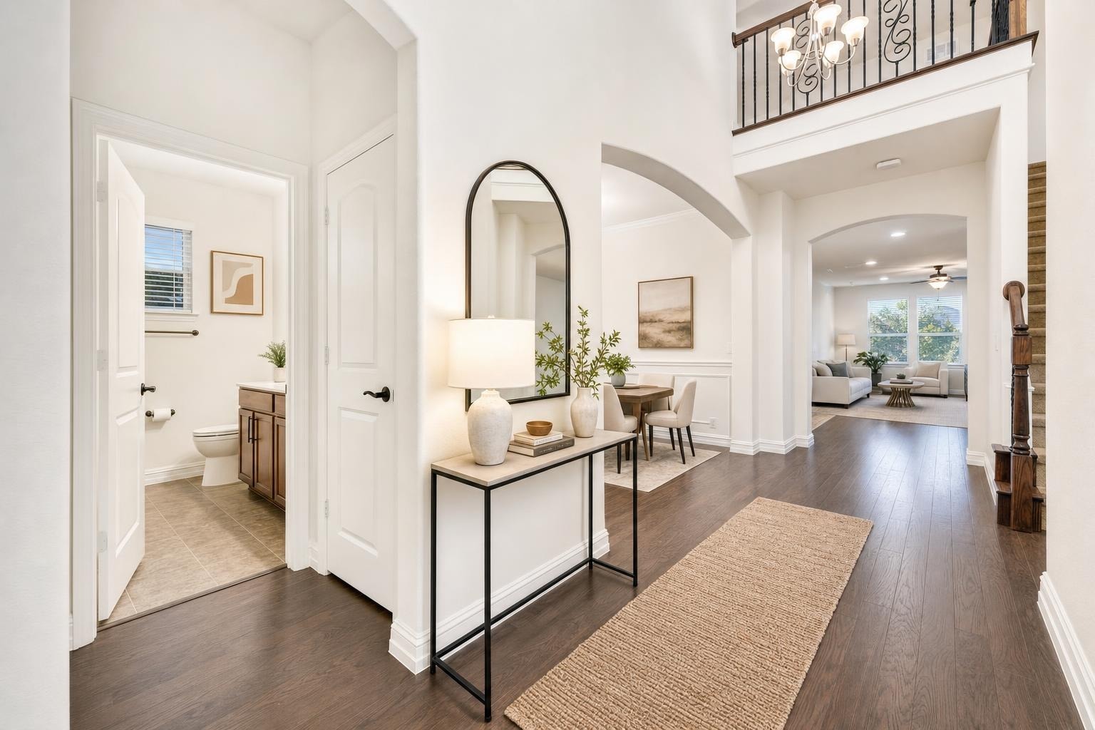 Modern entryway with dark wood floor, slim black metal and wood console table, arched mirror, lamp, vases, and beige rug.