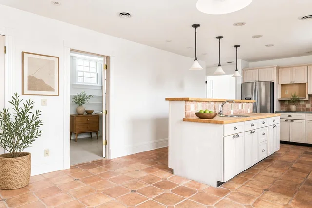 Modern kitchen with white cabinets, wood countertops, tiled floor, pendant lights, and a stainless steel refrigerator