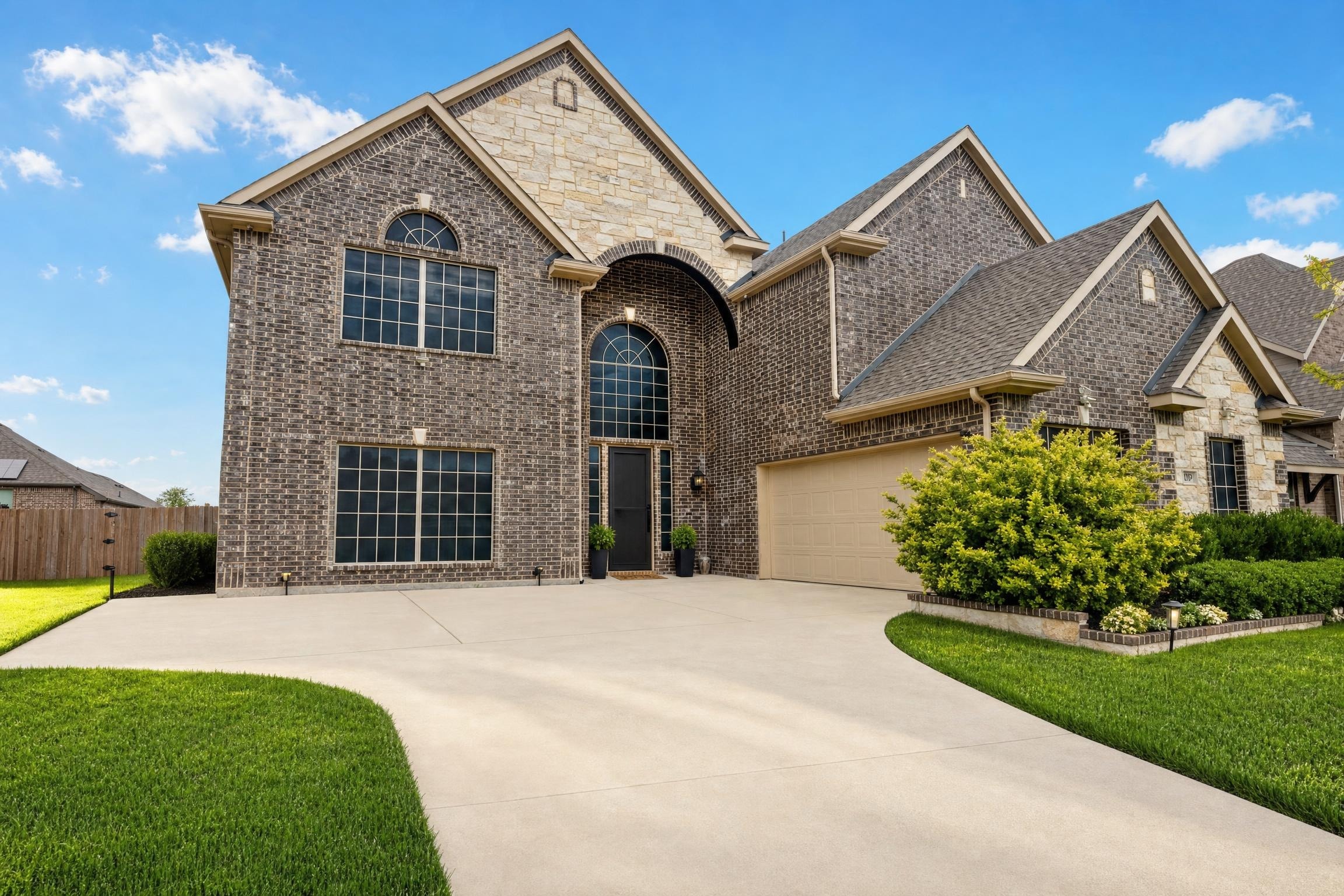 Large two-story brick and stone house with arched front door and windows, beige garage door, and manicured green lawn.