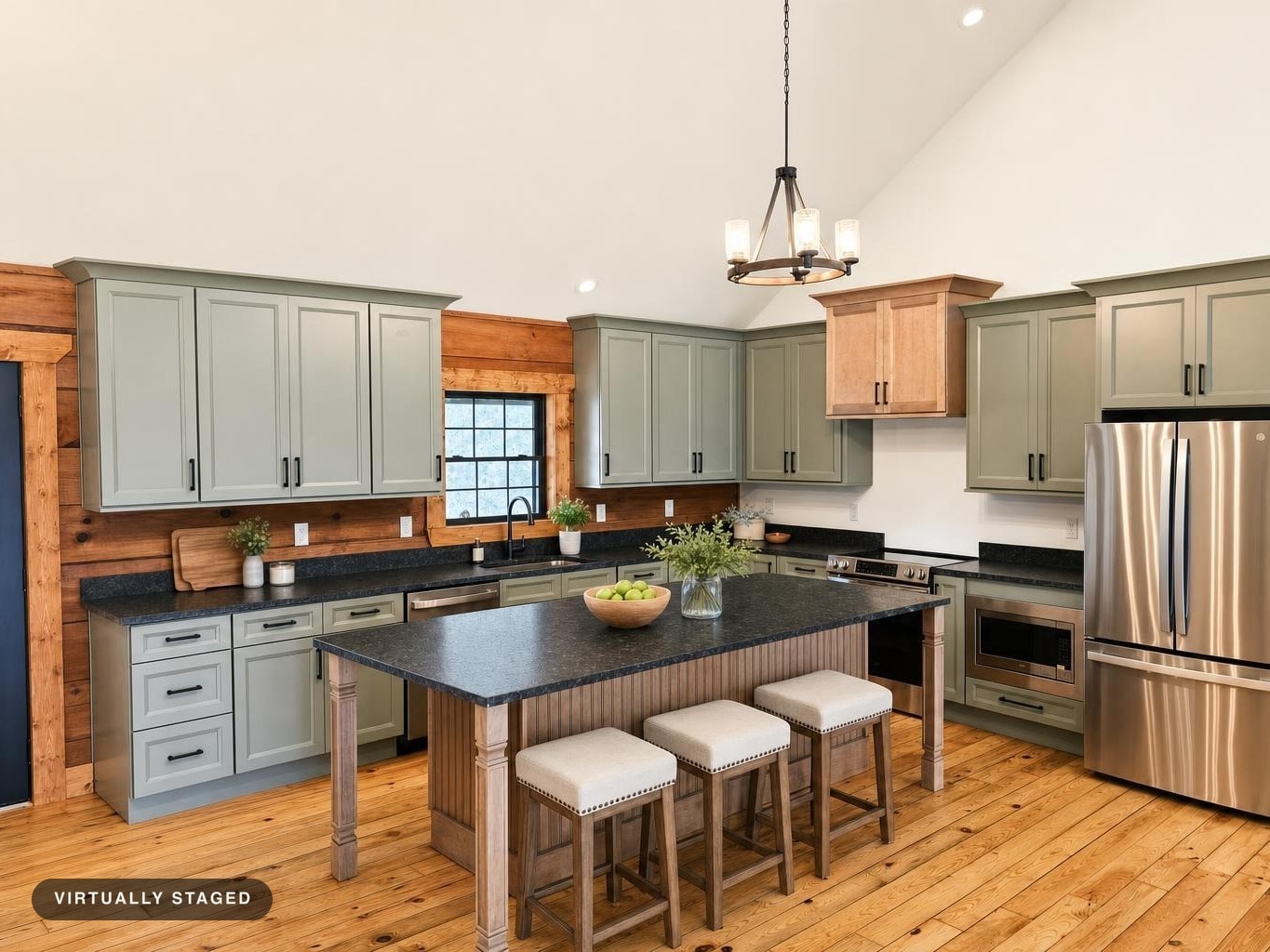 Modern rustic kitchen with sage gray cabinets, dark granite countertops, wooden floor, and three beige cushioned stools at the island.