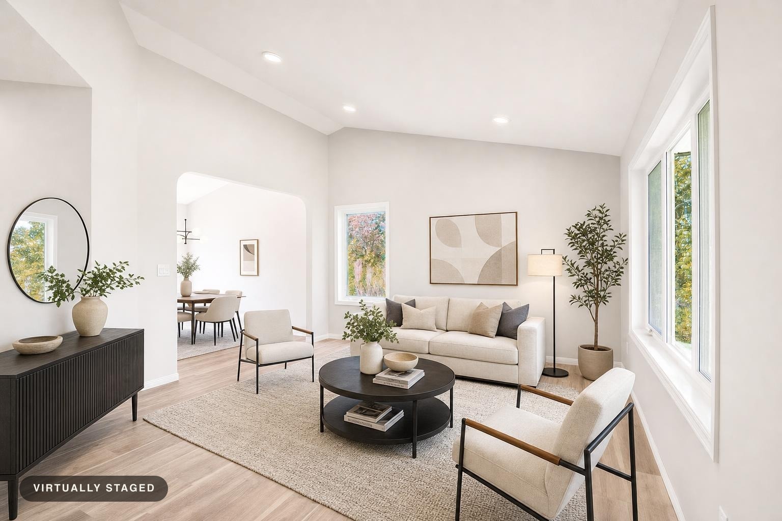 Bright modern living room with beige sofa, black metal framed chairs, round black coffee table, and a floor lamp near plant.