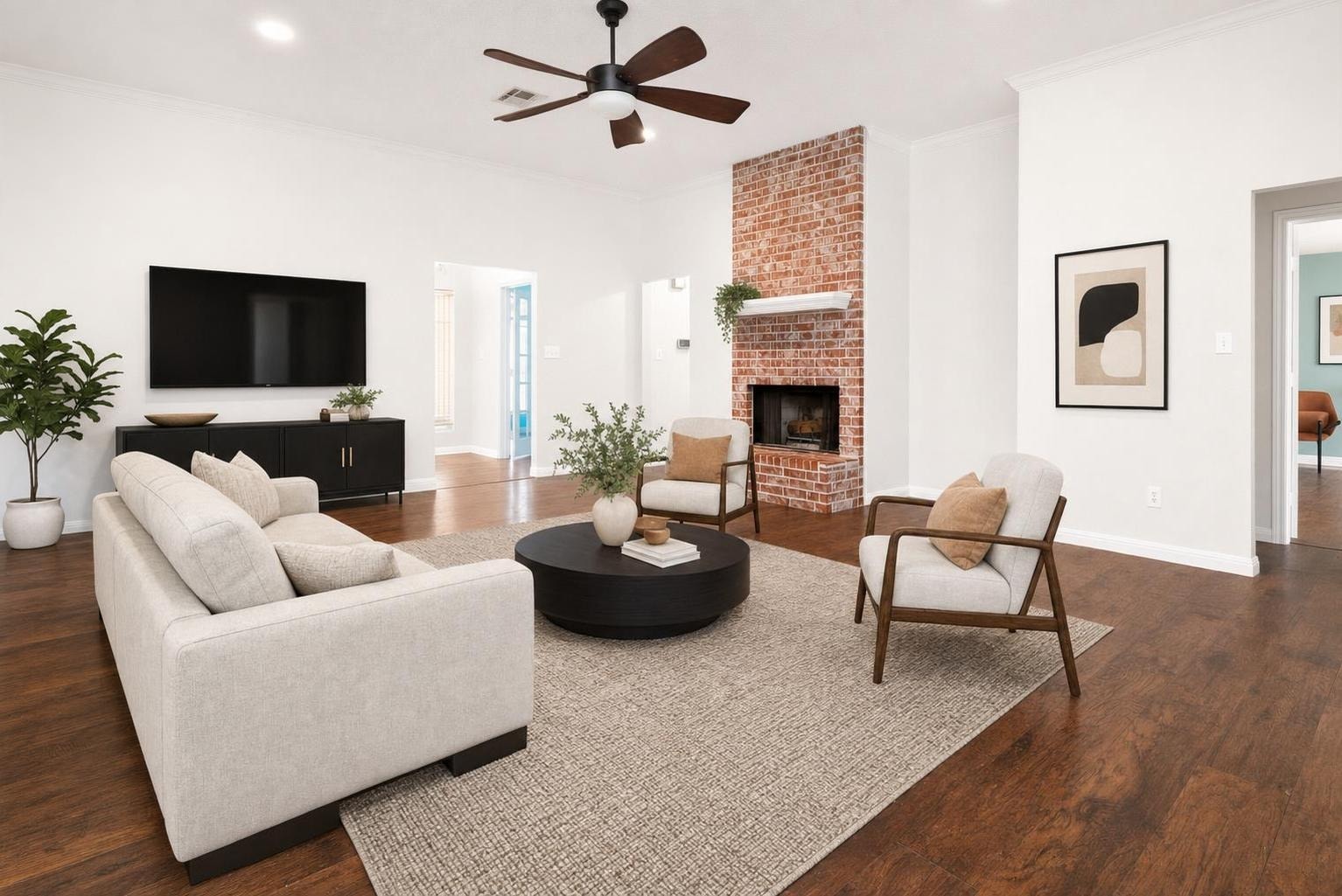 Bright modern living room with light beige sofa, two armchairs, round black coffee table, brick fireplace, and wood floor.